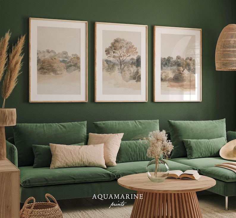 May include: Three framed landscape prints in neutral tones hang above a green velvet sofa. The prints depict trees and fields in a watercolour style. A round wooden coffee table and decorative items complete the scene.