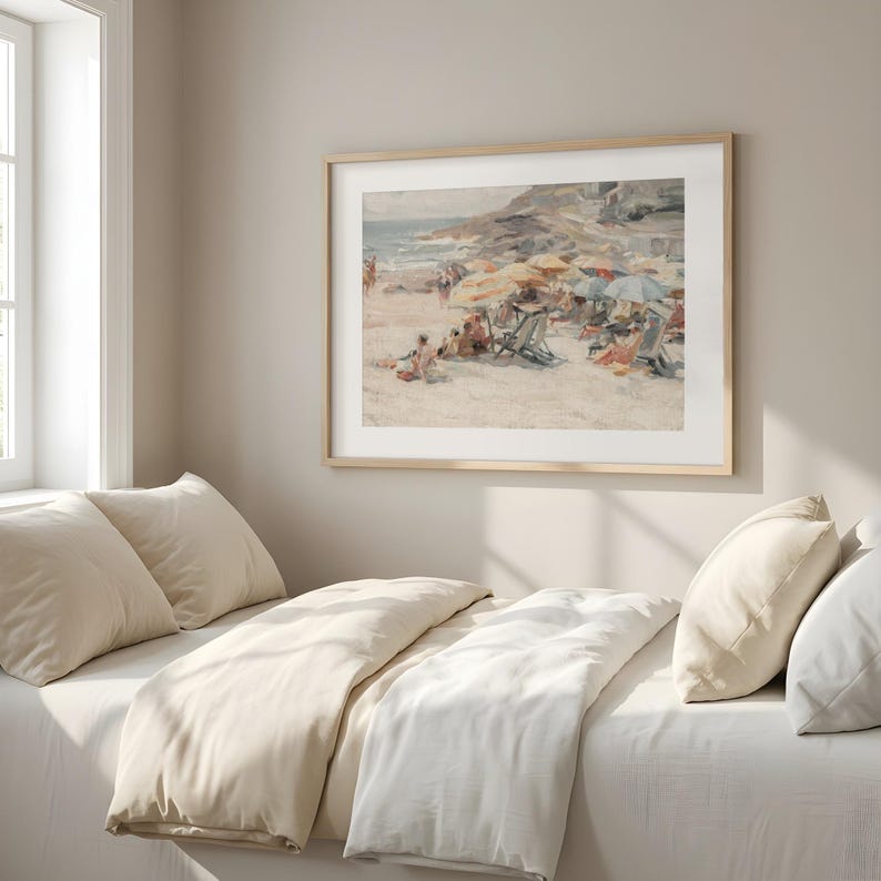 May include: A framed print of a beach scene with people, umbrellas, and beach chairs. The artwork has a vintage aesthetic, with soft colors and a focus on the beach and ocean. The frame is a light wood color.