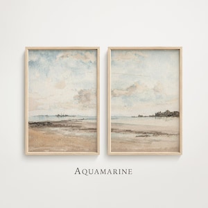 May include: Two framed watercolor prints depicting a serene coastal landscape. The artwork features a sandy beach, calm water, and a cloudy sky in shades of beige, blue, and brown. The word "AQUAMARINE" is printed in black at the bottom.