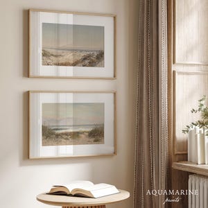 May include: Two framed landscape prints with beach scenes, displayed on a wall. The prints have light wood frames and are hung above a small, round table with an open book. The text "AQUAMARINE prints" is visible.