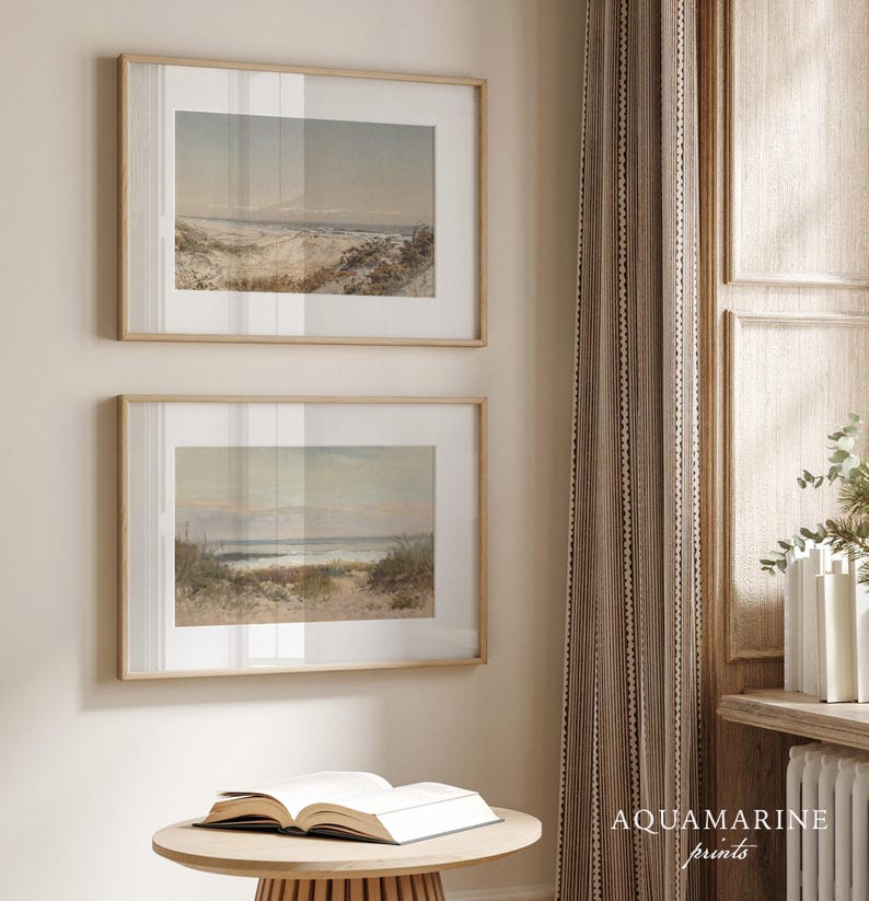 May include: Two framed landscape prints with beach scenes, displayed on a wall. The prints have light wood frames and are hung above a small, round table with an open book. The text "AQUAMARINE prints" is visible.