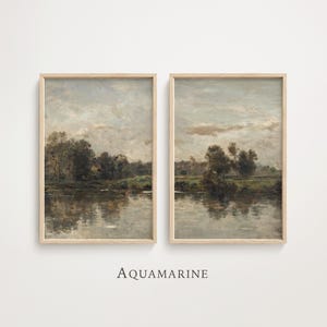 May include: Two framed landscape paintings with a serene river scene. The artwork features muted tones of gray, brown, and green, with reflections in the water. The frames are a light wood color. The word "AQUAMARINE" is printed below the paintings.