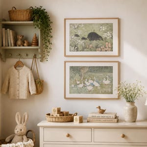 May include: A cozy nursery scene with a light green shelf holding books, wooden toys, and a hanging beige cardigan. Two framed nature prints and a dresser with a basket of blocks and a stuffed bunny complete the room's decor.