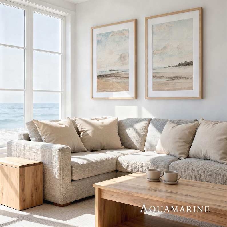 May include: A living room scene featuring a light gray sectional sofa with beige throw pillows. Two framed landscape art prints hang above the sofa. A wooden coffee table and side table complete the coastal decor. The text "AQUAMARINE" is visible.