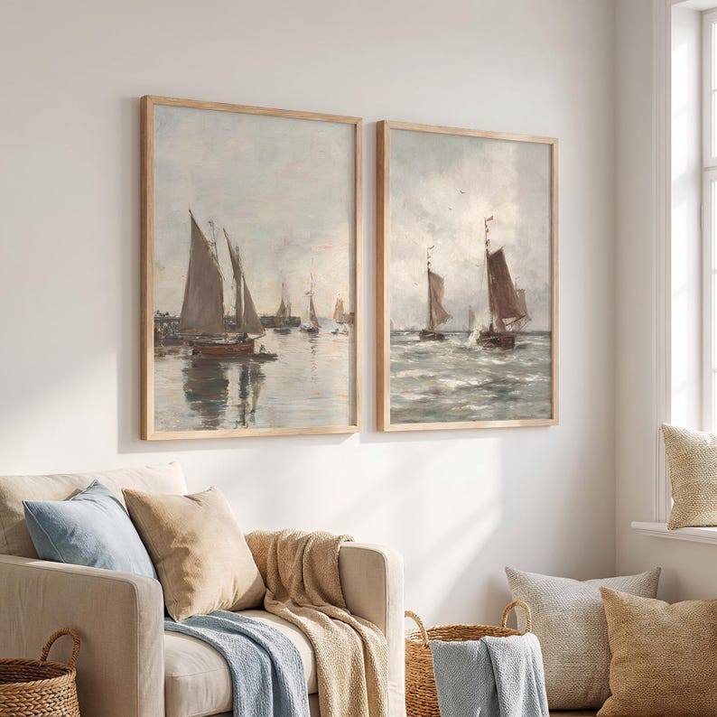May include: Two framed vintage-style prints depict sailboats on the water. The artwork features muted tones of gray, brown, and beige, with the boats' sails catching the light. The frames are a light wood color, adding to the classic aesthetic.