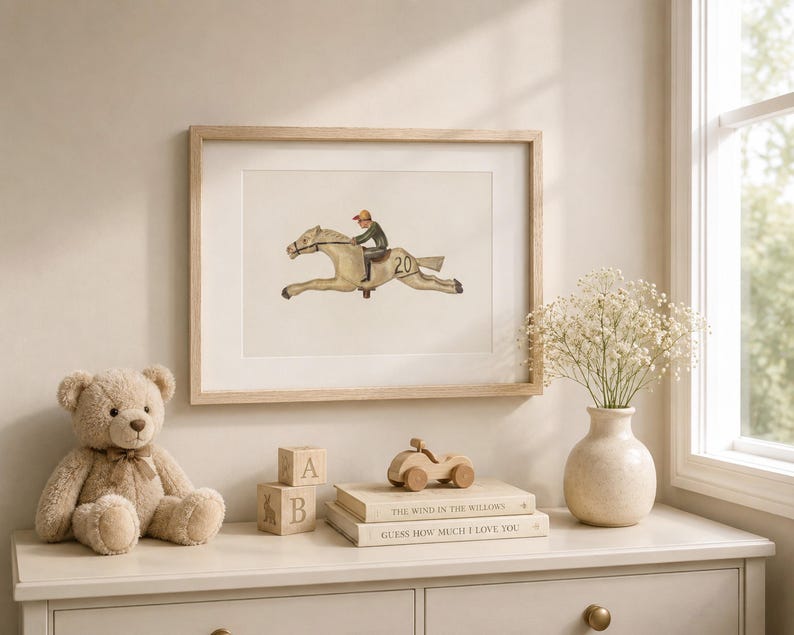 May include: A framed watercolour print of a horse and jockey in a race. The artwork is in a light wood frame and hangs above a chest of drawers. A teddy bear, wooden blocks, and books are on the chest of drawers.