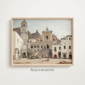 May include: A framed art print depicting a Mediterranean town square with a large church, a tall bell tower, and a central fountain. The scene features white buildings, stone stairs, and a mountain backdrop in muted tones of beige, gray, and terracotta.