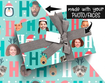Puede incluir: Un regalo envuelto con una cinta gris y una etiqueta blanca en blanco. El papel de regalo es azul claro con un patrón de caras, renos, pingüinos y la palabra "HO". También es visible el texto "made with your PHOTO/FACES".