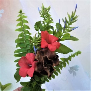 Pu&ograve; includere: Un mazzo di fiori rossi con foglie verdi e boccioli di fiori blu.