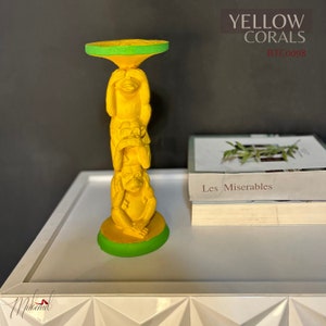 Può includere: Portacandele giallo con tre scimmie impilate l'una sull'altra. Le scimmie sono nella posa "Non vedere il male, non ascoltare il male, non parlare il male". Il portacandele ha un bordo verde ed è su una superficie bianca. Il testo "YELLOW CORALS BTC0098" è nell'angolo in alto a destra dell'immagine.