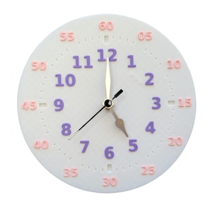 Puede incluir: Un reloj de pared redondo de color blanco con números de hora en morado del 1 al 12 y marcadores de minutos en rosa en incrementos de cinco, del 05 al 60. Tiene tres manecillas centrales, incluyendo un segundero negro y dos manecillas doradas.