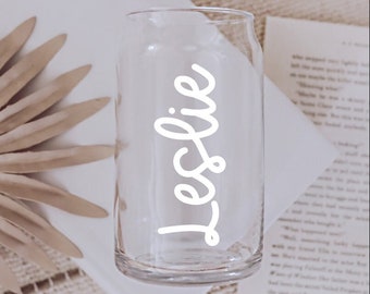 May include: A clear glass can with the name "Leslie" written in white cursive on the side.