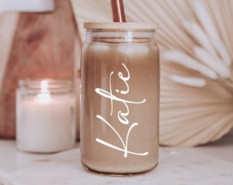May include: A glass jar with a bamboo lid and a copper straw, filled with a brown liquid. The jar has the name "Katie" written on it in white.