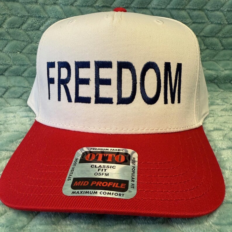 Puede incluir: Gorra de b&eacute;isbol blanca con visera roja. La palabra "FREEDOM" est&aacute; bordada en azul marino en la parte delantera. La gorra tiene un ajuste cl&aacute;sico y est&aacute; hecha con tela de primera calidad. La etiqueta dice "MID PROFILE" y "MAXIMUM COMFORT".