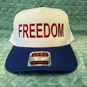 Puede incluir: Gorra de b&eacute;isbol blanca y azul con la palabra "FREEDOM" bordada en rojo. La gorra tiene un ajuste cl&aacute;sico y un perfil medio. Fabricada con tejido de primera calidad.