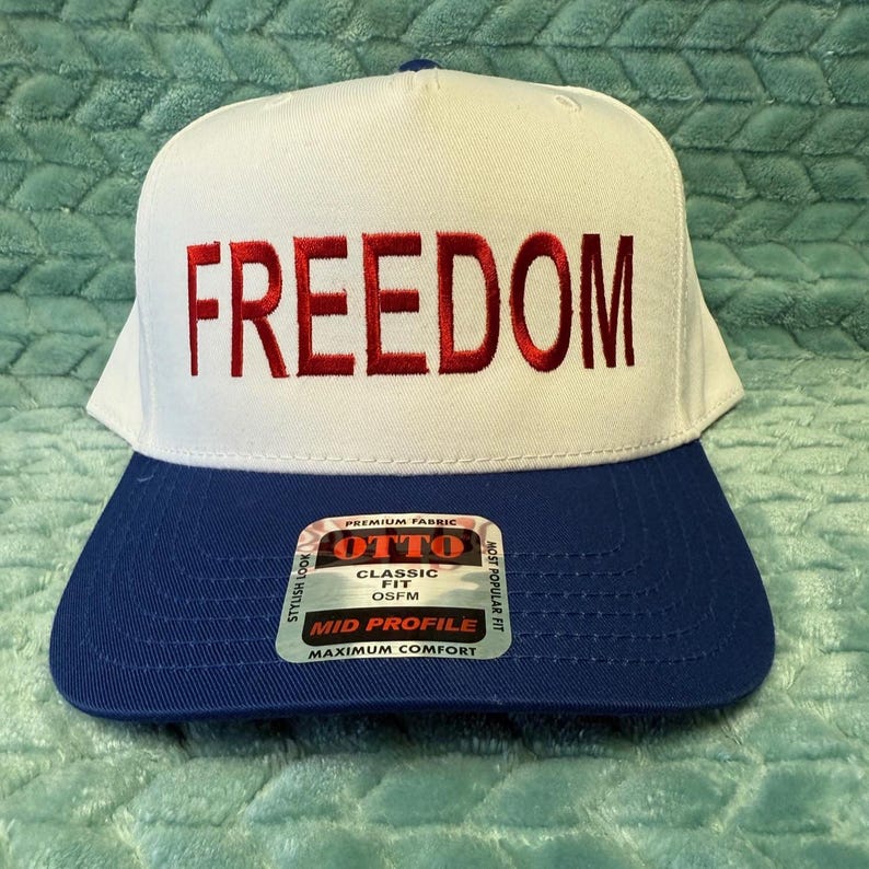 Puede incluir: Gorra de b&eacute;isbol blanca y azul con la palabra "FREEDOM" bordada en rojo. La gorra tiene un ajuste cl&aacute;sico y un perfil medio. Fabricada con tejido de primera calidad.