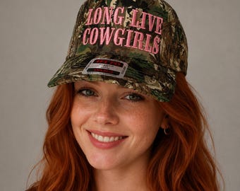 May include: A camouflage baseball cap featuring the embroidered text LONG LIVE COWGIRLS in pink thread on the front panel. The cap has a structured crown, a curved brim, and a small rectangular sticker on the brim with the text OTTO CLASSIC FIT.