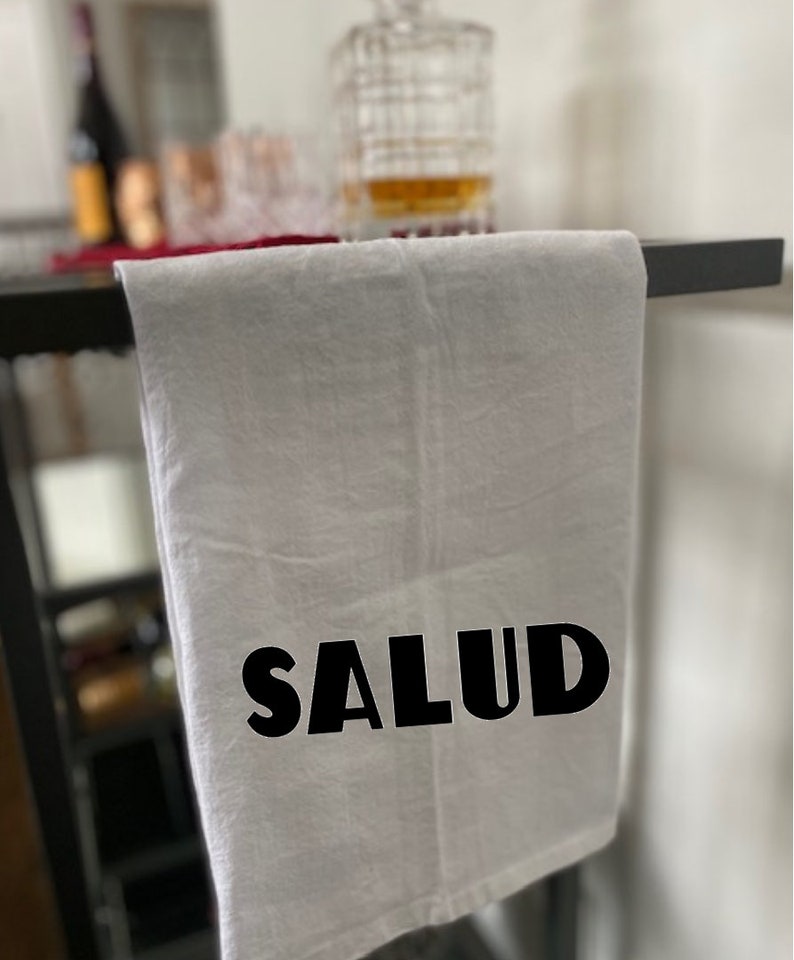 Puede incluir: Toalla de cocina blanca con la palabra "SALUD" impresa en letras negras en negrita.