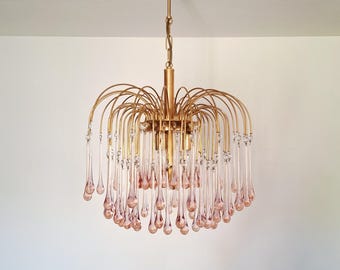 Könnte beinhalten: Eine goldfarbene Hängeleuchte mit einem kaskadierenden Design. Die Leuchte hat gebogene Arme und hängende rosa tropfenförmige Glasanhänger. Klare Kristallakzente sind eingearbeitet und sorgen für Glanz. Die Leuchte wird an einer Deckenhalterung aufgehängt.