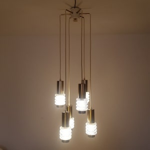 May include: A gold-toned chandelier with six clear glass light fixtures. The chandelier has a modern design and is hanging from the ceiling.