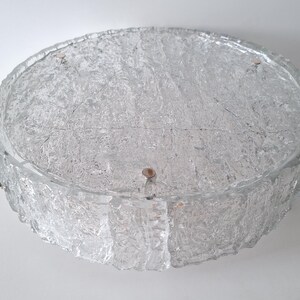 May include: A clear, round, textured glass ceiling light fixture. The fixture has a rough, icy appearance and is mounted with small, copper-colored rivets. The light is designed to be mounted flush against the ceiling.