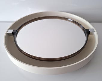 Puede incluir: Un espejo redondo blanco de pared con un diseño giratorio. El espejo tiene un marco de plástico marrón oscuro y un acento de metal plateado.