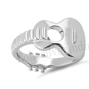 Puede incluir: Anillo de guitarra de plata con un diseño detallado. El anillo está hecho de plata y tiene la forma de una guitarra con un agujero en el medio. El anillo es un gran regalo para los amantes de la música.