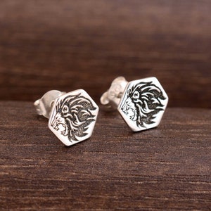 May include: A pair of silver stud earrings with a hexagonal design featuring a lion's head in black.