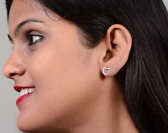 May include: A close-up of a person's ear wearing a pair of silver cat-shaped stud earrings.