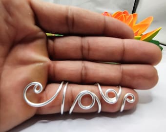May include: Five silver wire rings, each shaped like a letter, spelling out the word "love", worn on a person's fingers.