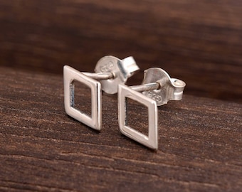 May include: A pair of silver square stud earrings with a hollow center. The earrings are on a wooden surface.