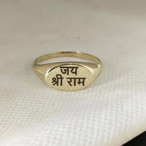 May include: A gold signet ring with the inscription "जय श्री राम" in black lettering.