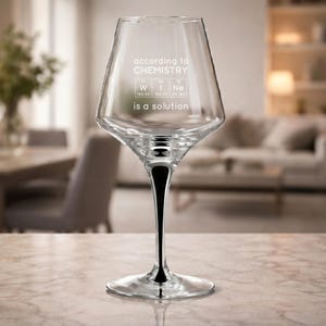 May include: A clear wine glass with a black stem. The glass has the text "according to CHEMISTRY" and "is a solution" with the periodic table symbols for wine. The glass is on a marble surface.