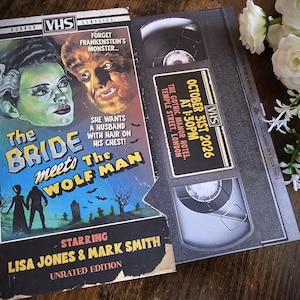 May include: A vintage VHS tape for the horror film "The Bride Meets The Wolf Man," featuring a Bride of Frankenstein and Wolfman graphic. The tape is open, revealing the interior and a label with event details.