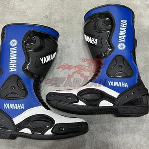 Puede incluir: Par de botas de moto Yamaha azules, negras y blancas. Las botas tienen el logotipo y el texto de Yamaha en blanco. Cuentan con paneles protectores y una suela reforzada. Botas diseñadas para la conducción y las carreras de motos.