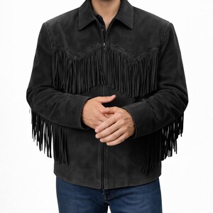 May include: A black suede jacket with fringe detailing across the chest, shoulders, and sleeves. The jacket has a collared neckline and a full-length zipper. The model is wearing blue jeans. This western-style jacket is a statement piece.