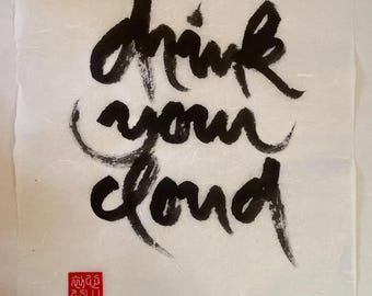 May include: Calligraphy art print on textured paper. The black ink script reads "Drink your cloud." A small red square seal is in the lower left corner. The paper has a subtle, off-white color.