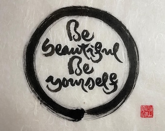 May include: Black ink calligraphy on a white background with a black circle around the words "Be beautiful Be yourself".