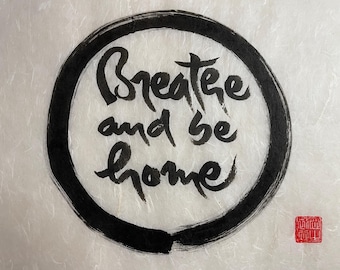 May include: Black ink calligraphy on white paper in a circle with the words "Breathe and be home".