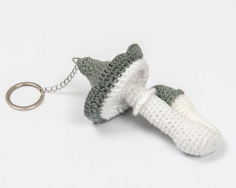 May include: A crocheted mushroom keychain with a white stem and a green and white cap. The keychain has a silver metal ring.