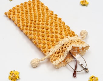 May include: A crocheted yellow and white eyeglass case with a tassel and a pair of glasses inside.