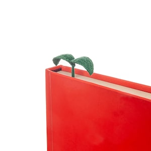 May include: A red hardcover book with a green plant bookmark. The bookmark is made of felt and has two leaves.