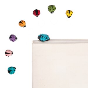 May include: A collection of colorful crocheted ladybugs, some are on a white surface, and one is on top of a white book.