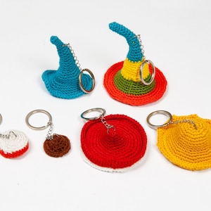 May include: Six crocheted hat keychains in various colors, including red, yellow, blue, and green. The hats are attached to silver key rings.