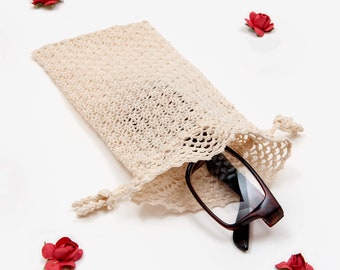 May include: A crocheted beige eyeglass case with a drawstring closure, holding a pair of brown reading glasses. The case is surrounded by small red flowers.