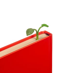May include: A red hardcover book with a green plant bookmark sticking out of the top.