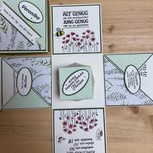Könnte beinhalten: Eine grüne und weiße Explosionsbox mit floralem Design. Die Box ist geöffnet und das Innere ist mit einem grünen und weißen Blumenmuster verziert. Die Box hat eine kleine, weiße Box im Inneren mit dem Text "Hab immer Sonne im Herzen". Die Box ist mit einer Biene und Blumen verziert.
