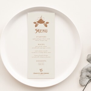 May include: A beige menu card with a brown illustration of a pumpkin and leaves. The text on the card reads "MENU", "STARTERS", "MAINS", "DESSERTS", and "CHARLOTTES BABY, BROOME".