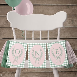 Puede incluir: Una pancarta de silla alta a cuadros verdes y blancos con círculos rosas y herraduras verdes con las letras O, N y E en el centro de cada círculo. La pancarta tiene borlas rosas y verdes.