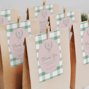 Puede incluir: Bolsas de regalo de vichy verde y blanco con etiquetas de agradecimiento rosas y verdes. Las etiquetas presentan una corona con la letra E y el texto "Gracias por hacer que este día sea tan especial".